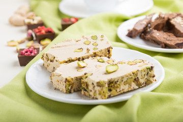 traditional arabic sweets sesame halva with chocolate and pistachio and a cup of coffee on green textile background. side view, selective focus.