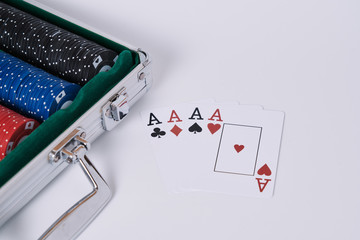 Game cards. Four cards, four aces, four symbols in background and white table and poker chips briefcase in the frame.