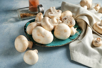 Plate with fresh mushrooms on color background