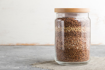 glass jar with buckwheat poured in layers on a gray and white background. side view