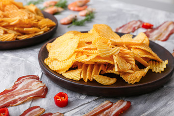 Plate with tasty potato chips and bacon on table