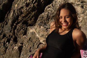 Young hipster woman lying on the rocks in a swimsuit over beach towel. Young woman lying near the sea with vintage sunglasses.