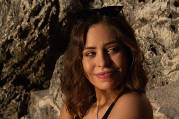Young hipster woman lying on the rocks in a swimsuit over beach towel. Young woman lying near the sea with vintage sunglasses.