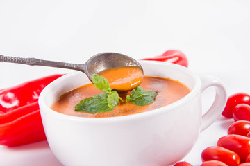 Gazpacho soup with some tomatoes and sweet pepper on a white background with a vintage spoon