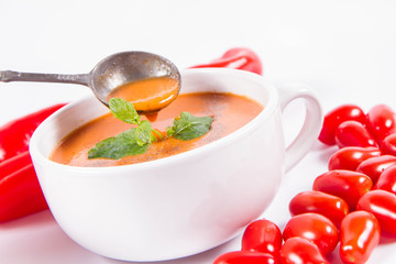 Gazpacho soup with some tomatoes and sweet pepper on a white background with a vintage spoon