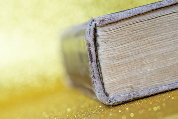 The spine of a thick old book lying on a yellow golden background. Library archive. History and...