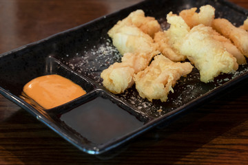 Golden deep fried Calamari on black plate with sea salt and spicy sauce.