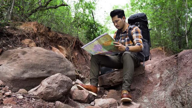 man traveler with backpack sitting and reading map in the natural forest