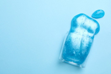 Overturned plastic container with bright slime on light blue background, top view. Space for text
