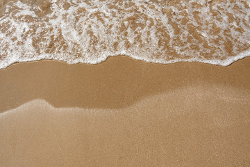 Fototapeta na wymiar Sea wave with white bubbles blow toward a sand beach