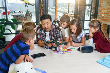 In physics and mechanics lesson young Asian teacher demonstrates quadcopter for caucasian pupils at...