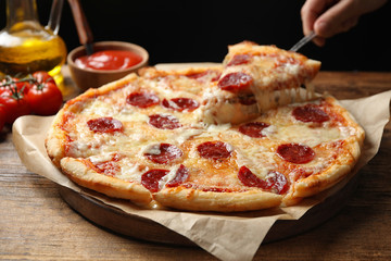 Woman taking slice of tasty pepperoni pizza at wooden table, closeup
