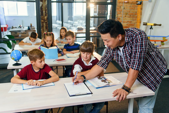 Pupils sit at desks and listens to the teacher while he explaining the topic of new lesson.