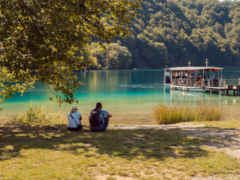 Pareja de turistas mirando el barco con pasajeros amarrado en el muelle en el Parque Nacional de Plitvice en Croacia, verano de 2019