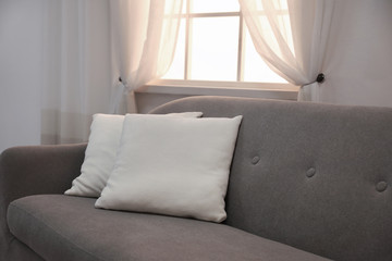 Modern comfortable sofa with pillows near window indoors. Stylish interior