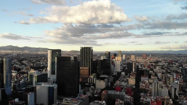 Aerial of the skyline in Paseo de la Reforma, Mexico City, during sunset. Drone flying forward with a blue sky as background. CDMX