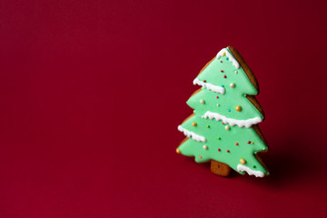 gingerbread cookie of green Christmas Tree on red background. Traditional Christmas food. Christmas and New Year holiday concept. Copyspace