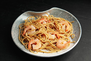 Plate of tasty buckwheat noodles with shrimps on black table