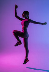 Sporty young woman jumping isolated on purple light background