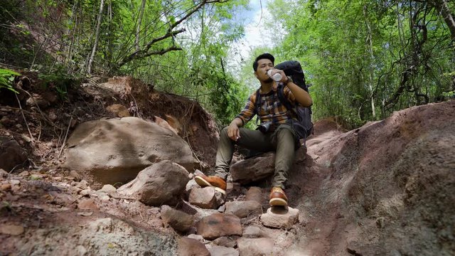 tired man traveler with backpack resting and dirking water in the natural forest