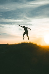 silhouette of young man jumping on sunset background of blue sky