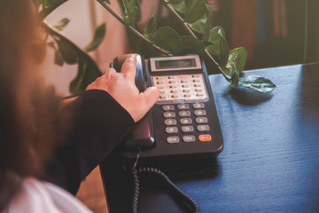 Mano di donna che sta per prendere la cornetta di un vecchio telefono aziendale poggiato su una...