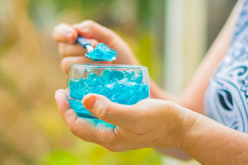 Close of old woman's hands with a jar of desserts in hand eating blue jelly