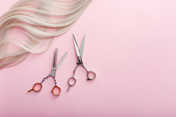 Scissors and other hairdresser's accessories and strand of blonde hair on pink background. Flat lay with space for text. Hairdresser service. Beauty salon service