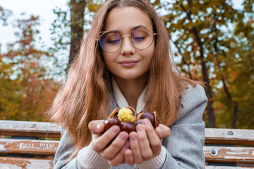 Beautiful girl is smiling and holding chestnuts in her hands outdoors in fall