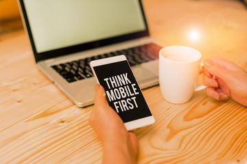 Writing note showing Think Mobile First. Business concept for Easy Handheld Device Accessible Contents 24 or7 Handy woman with laptop smartphone and office supplies technology