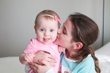 Close up Portrait of Two Sisters, Cute 8 Month Old baby Girl with Big blue Eyes and 8 Years Old School Age Girl With Brown Eyes , Happy Baby Girl