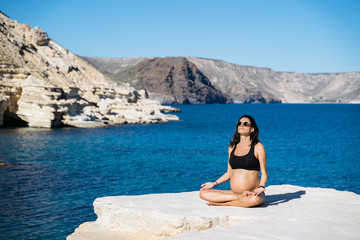 Young pregnant woman practicing yoga next to the mediterranean sea