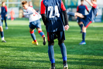 Boys in white and blue sportswear plays  football on field, dribbles ball. Young soccer players with ball on green grass. Training, football, active lifestyle for kids concept 