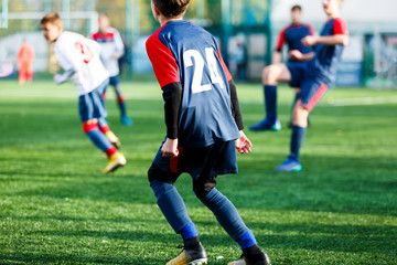 Boys in white and blue sportswear plays  football on field, dribbles ball. Young soccer players with ball on green grass. Training, football, active lifestyle for kids concept 