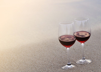 Two wine glasses with red wine on sand on the beach. Valentine's Day concept.