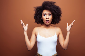 pretty young african american woman with curly hair posing cheerful gesturing on brown background, lifestyle people concept