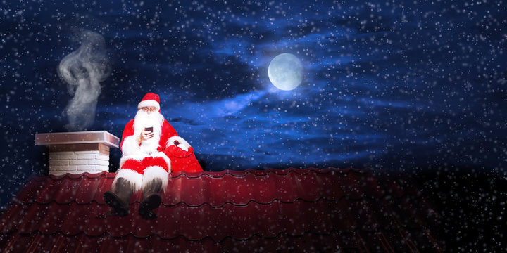 Santa Claus On The Roof Of A House With Tablet.