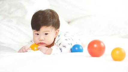 Cute baby lying on a white bed with a colorful ball.
