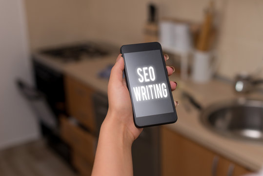 Conceptual hand writing showing Seo Writing. Concept meaning grabbing the attention of the search engines using specific word woman using smartphone and technological devices inside the home