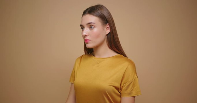 Brunette woman in yellow t shirt happy laughs lookong at camera isolated on beige background.