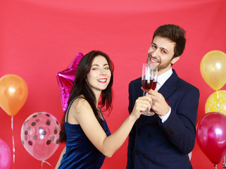 Portrait of smart man and beautiful woman holding and drinking glass of wine isolated on red background with colorful balloons - Christmas and Happy New Year party concept