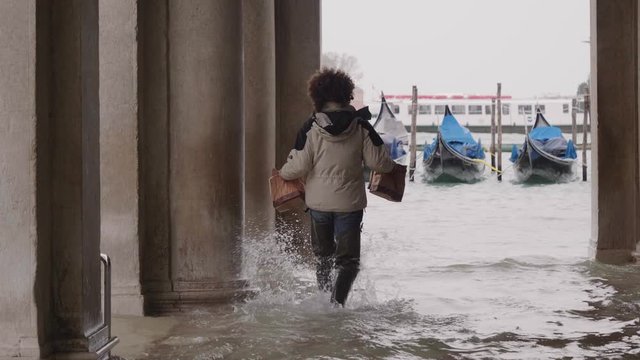 VENICE, ITALY - November 12, 2019: Man delivering food walking on the flooded streets (acqua alta) in Venice, Italy. Venice high water. 4k