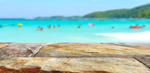 Brown stone table top with blurred people at the beach