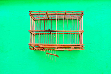 An empty bird cage on a green wall.
