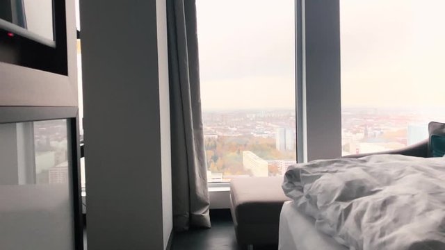Best view of the city from the modern hotel room in Germany. A luxury hotel room with big windows on the highest floor in the big town. Bed with white sheets and tv in the apartment with a great view.
