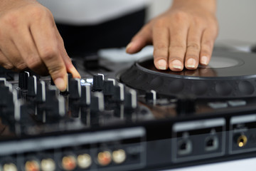 Hands of DJ mixing tracks on professional sound mixer.Fashionable rings on fingers of girl disc jockey playing music.Closeup,knobs and regulators in focus.Girl dj play music tracks at house party