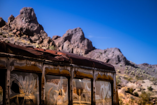 Abandoned, rusty bus in desert with mountains in the background