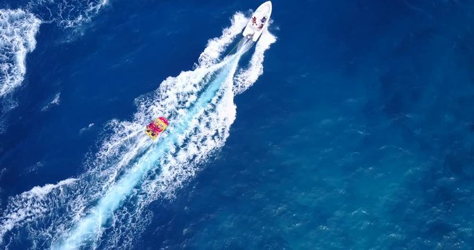 Water sport activities on clear blue sea of Malaysia, power boat push tow tube with tourists on board followed by ski jet tracing beautiful white footprint