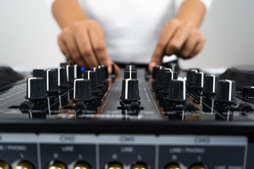 Hands of DJ mixing tracks on professional sound mixer.Fashionable rings on fingers of girl disc jockey playing music.Closeup,knobs and regulators in focus.Girl dj play music tracks at house party
