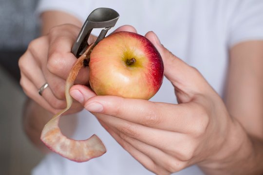 young woman in white shirt peeling an apple with a peeler